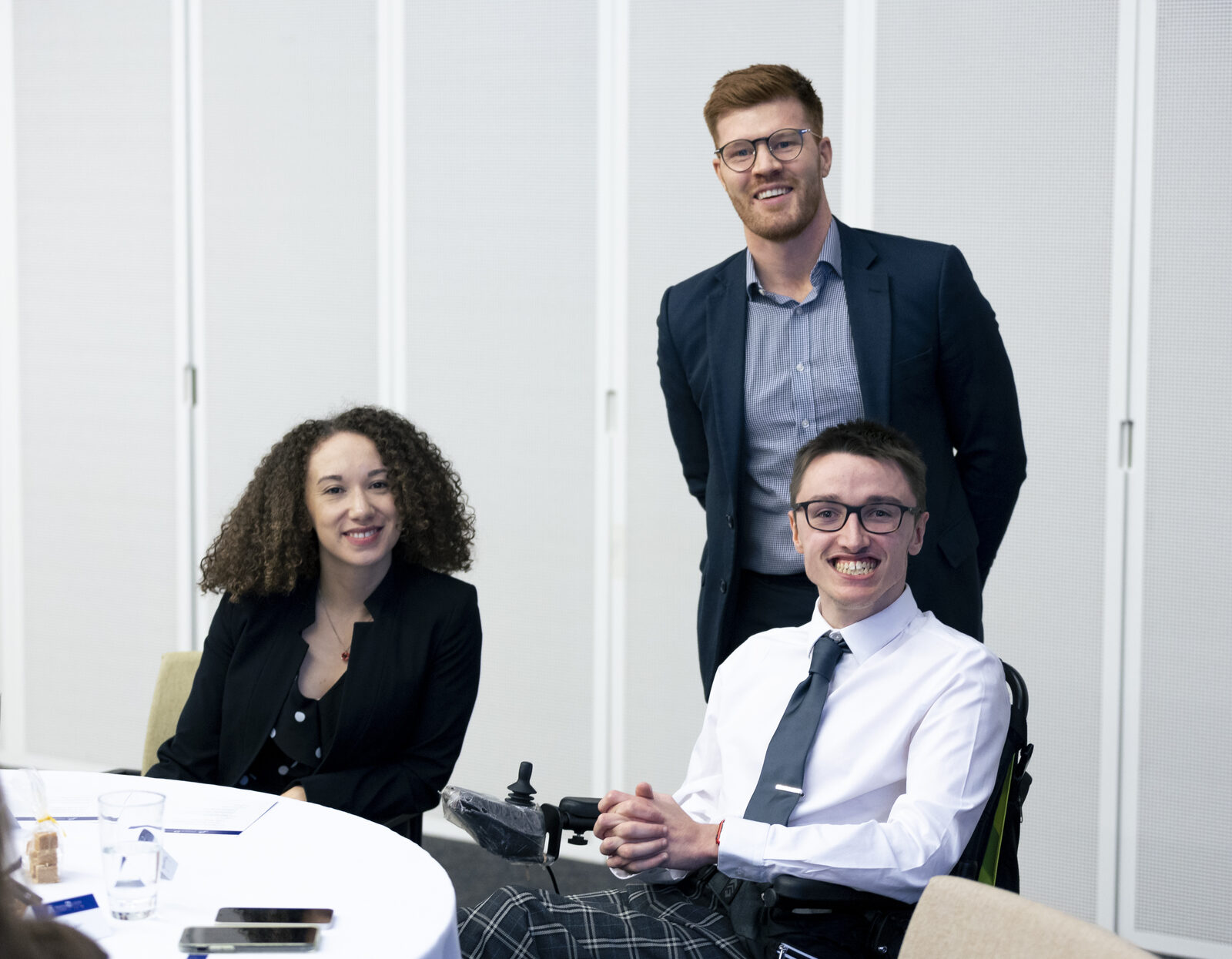 Three people from Housing Options Scotland smiling together at a table, one of them a wheelchair user